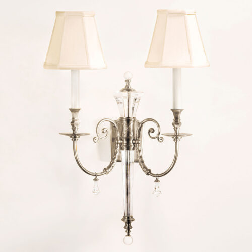 Two-light electrified solid brass and crystal sconce with lacquered silver-plated finish. Wall sconce has graceful scrolled arms and classic piped fabric shades